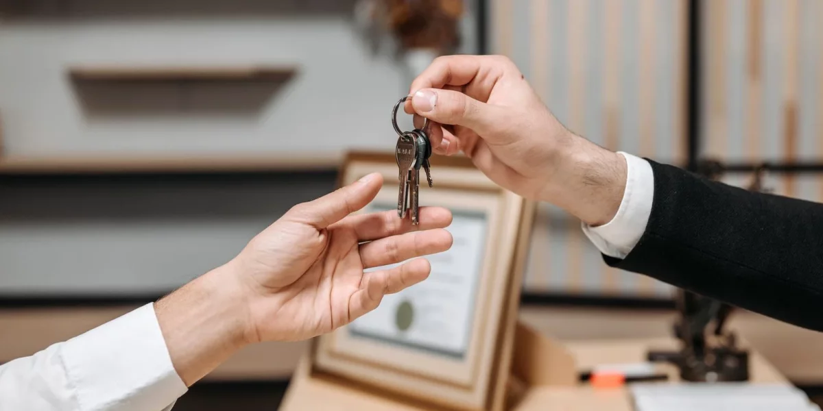 Mains échangeant un trousseau de clés au-dessus d'un bureau : le bailleur remet les clés du logement à son locataire