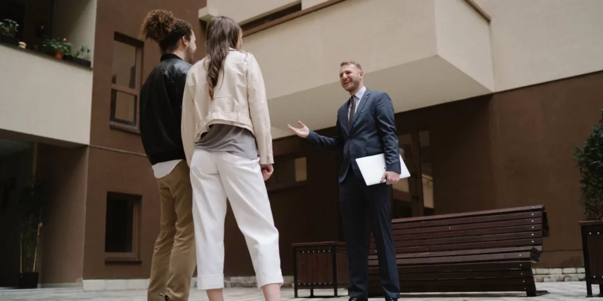Agent immobilier discutant avec un couple devant un immeuble moderne — investissement-locatif