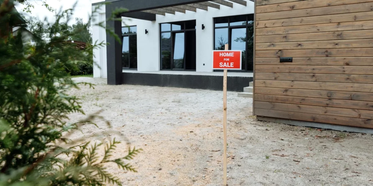 Maison moderne avec panneau "À vendre" dans un jardin — exoneration plus-value immobiliere