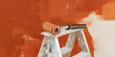 Rouleau de peinture orange sur une échelle en bois — peinture