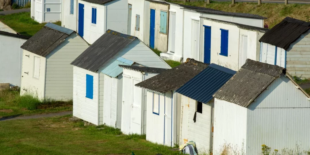 Bâtiments de plage colorés alignés sur un terrain herbeux — cabanisation