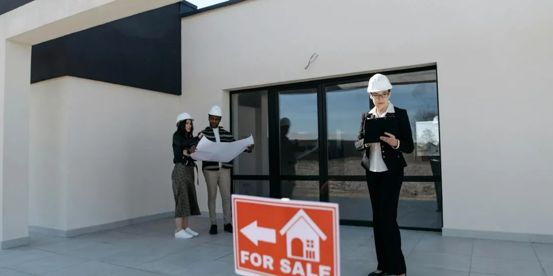Professionnels de l'immobilier avec plans devant une maison à vendre — marché