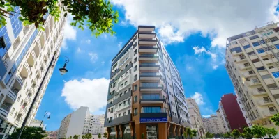 Immeuble moderne au coin d'une rue ensoleillée avec voitures stationnées — fnaim