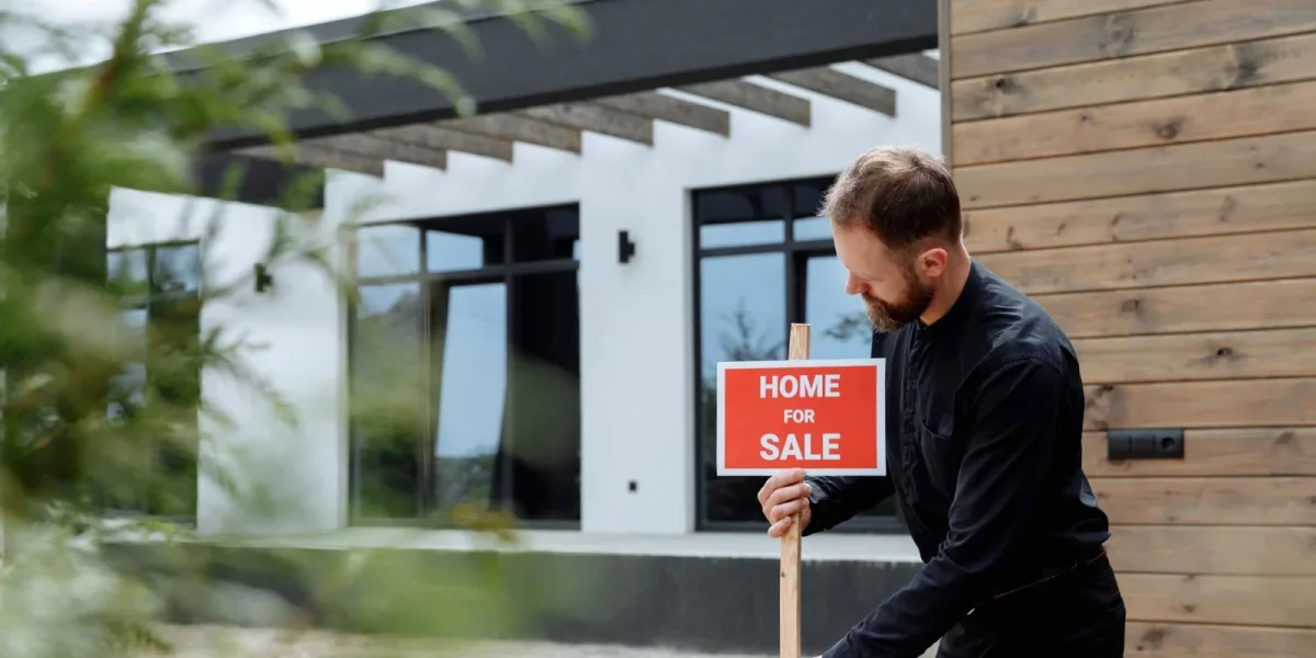 Homme tenant un panneau "À vendre" devant une maison moderne — prix-immobilier