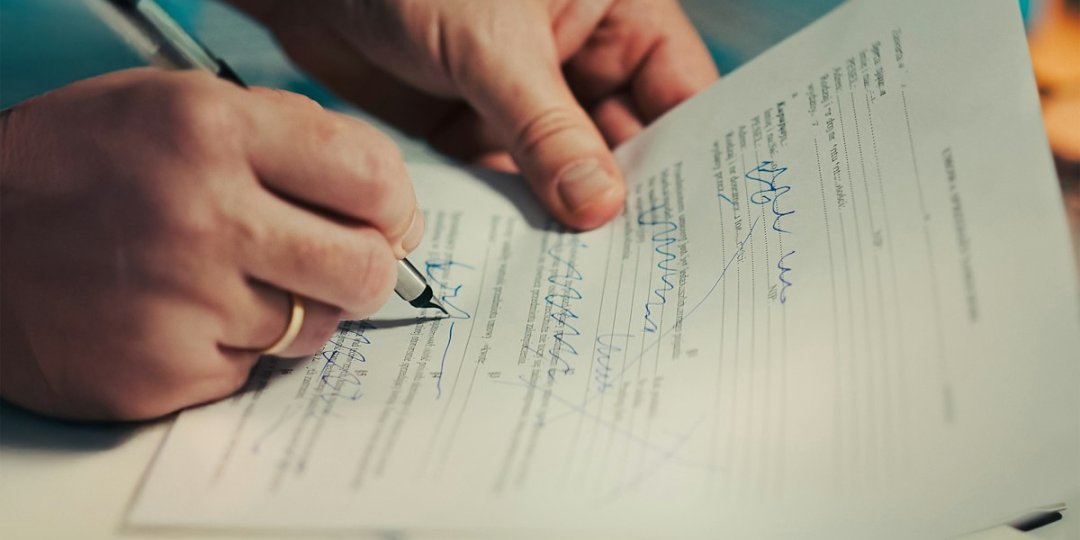 Signature d'une promesse de vente devant notaire — main tenant un stylo sur un document officiel