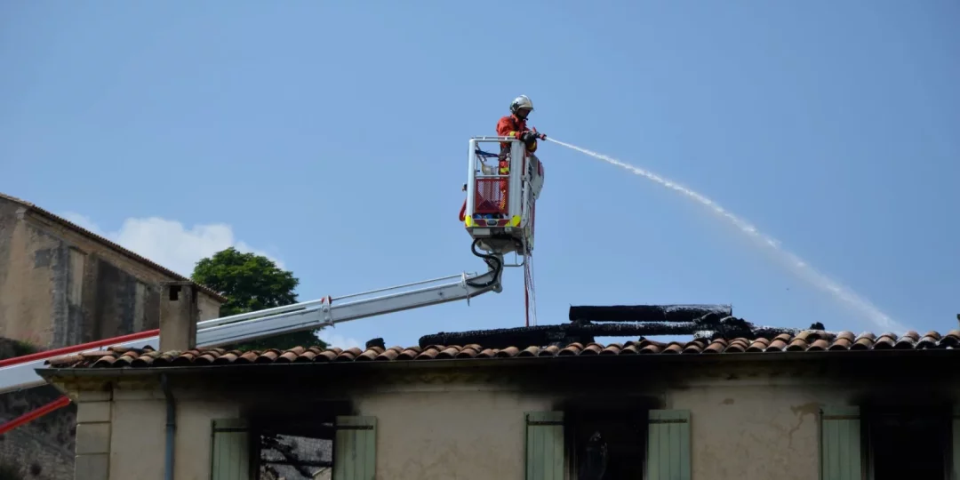 Pompier utilisant une échelle pour éteindre un feu sur un toit — incendie