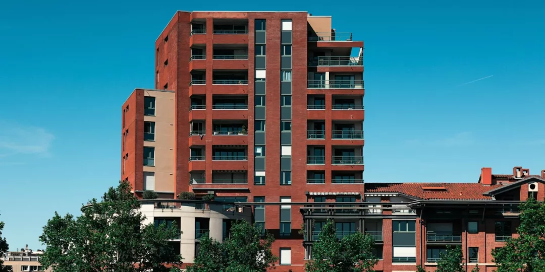Immeuble moderne en briques rouges avec balcons et arbres au premier plan — Toulouse