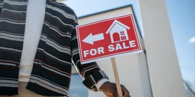 Homme tenant un panneau "à vendre" devant une maison moderne — vendre sa maison à un promoteur