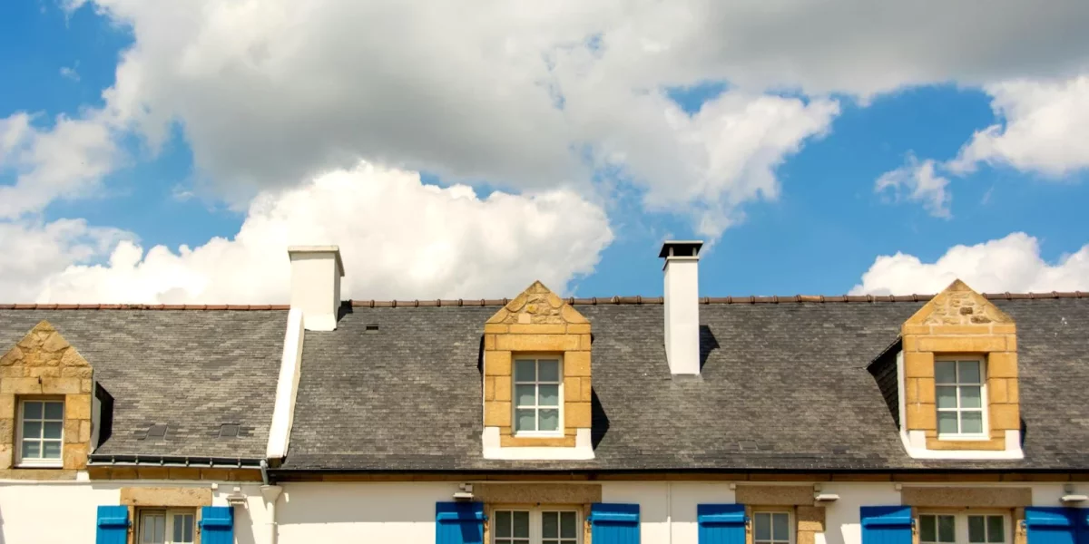 Toit de maisons avec volets bleus sous un ciel nuageux — maisons-pierre